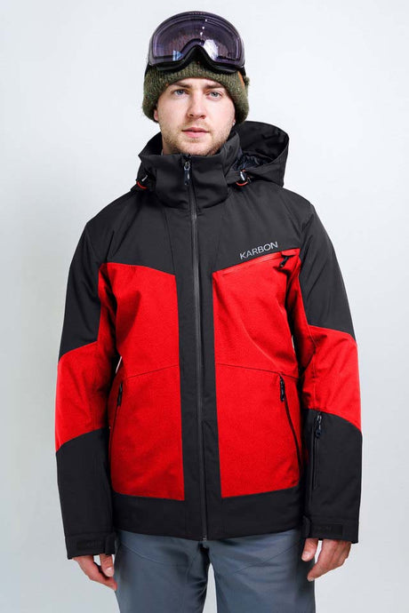 OrionMensInsulatedJacket-A man wearing a red and black Karbon ski jacket, a green knit beanie, and ski goggles, standing against a light gray studio background.