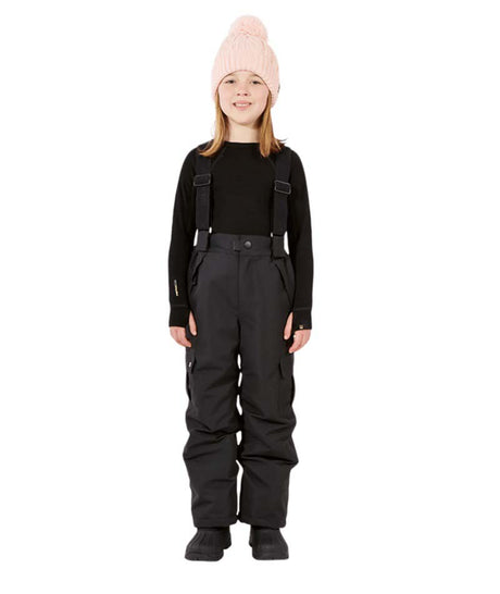 PlutoIIKidsPant-A child model wearing black snow bib overalls with suspenders, a black long-sleeve top, and a light pink knit beanie, standing against a solid white background.
