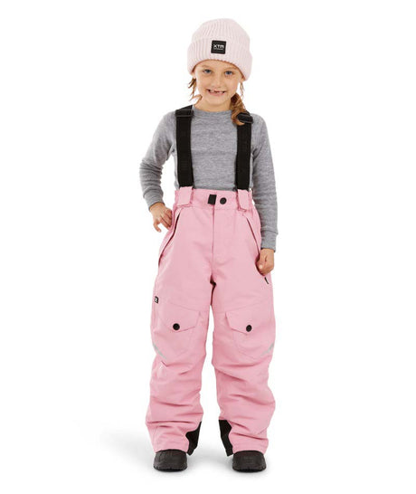 PlutoIIKidsPant-A young child wearing pink snow pants with black suspenders, a gray long-sleeve shirt, a light pink beanie, and black boots, standing against a plain white background.