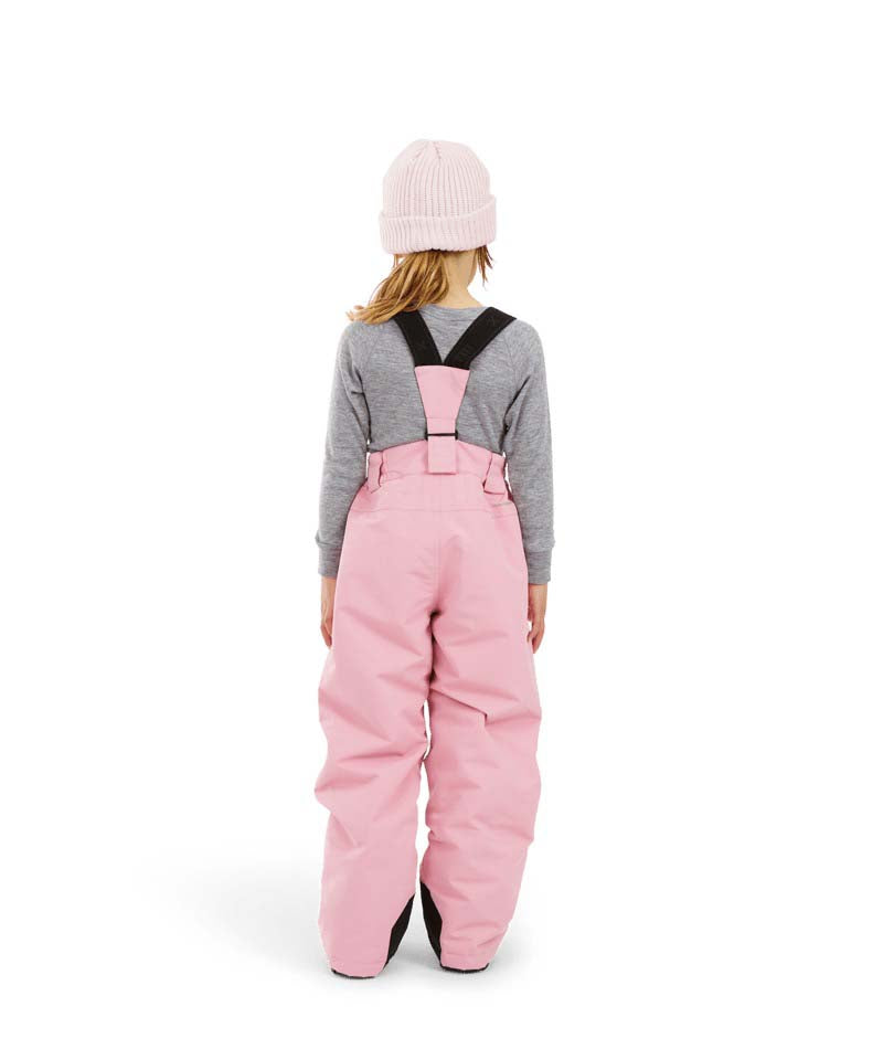 PlutoIIKidsPant-A child shown from the back wearing pink snow bib overalls with black shoulder straps, a gray long-sleeve shirt, and a light pink beanie on a white studio background.