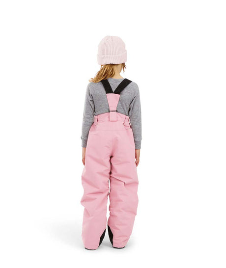 PlutoIIKidsPant-A child shown from the back wearing pink snow bib overalls with black shoulder straps, a gray long-sleeve shirt, and a light pink beanie on a white studio background.
