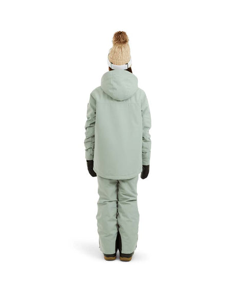RumbleJacket- A smiling girl wearing a light sage green snowboard jacket, matching snow pants, black gloves, and a knit beanie with ski goggles, standing against a plain white background.