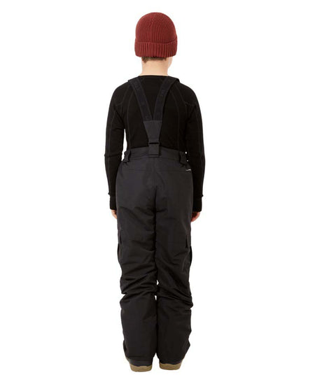 ScoobieIIPant-A child model wearing black snow bib overalls with suspenders, a black long-sleeve shirt, black snow boots, and a burgundy knit beanie, standing against a solid white background.
