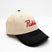 ScriptCap-A baseball cap with a cream-colored crown and a black curved brim, featuring the word 'Public' embroidered in red script on the front. The cap is photographed on a seamless white background.