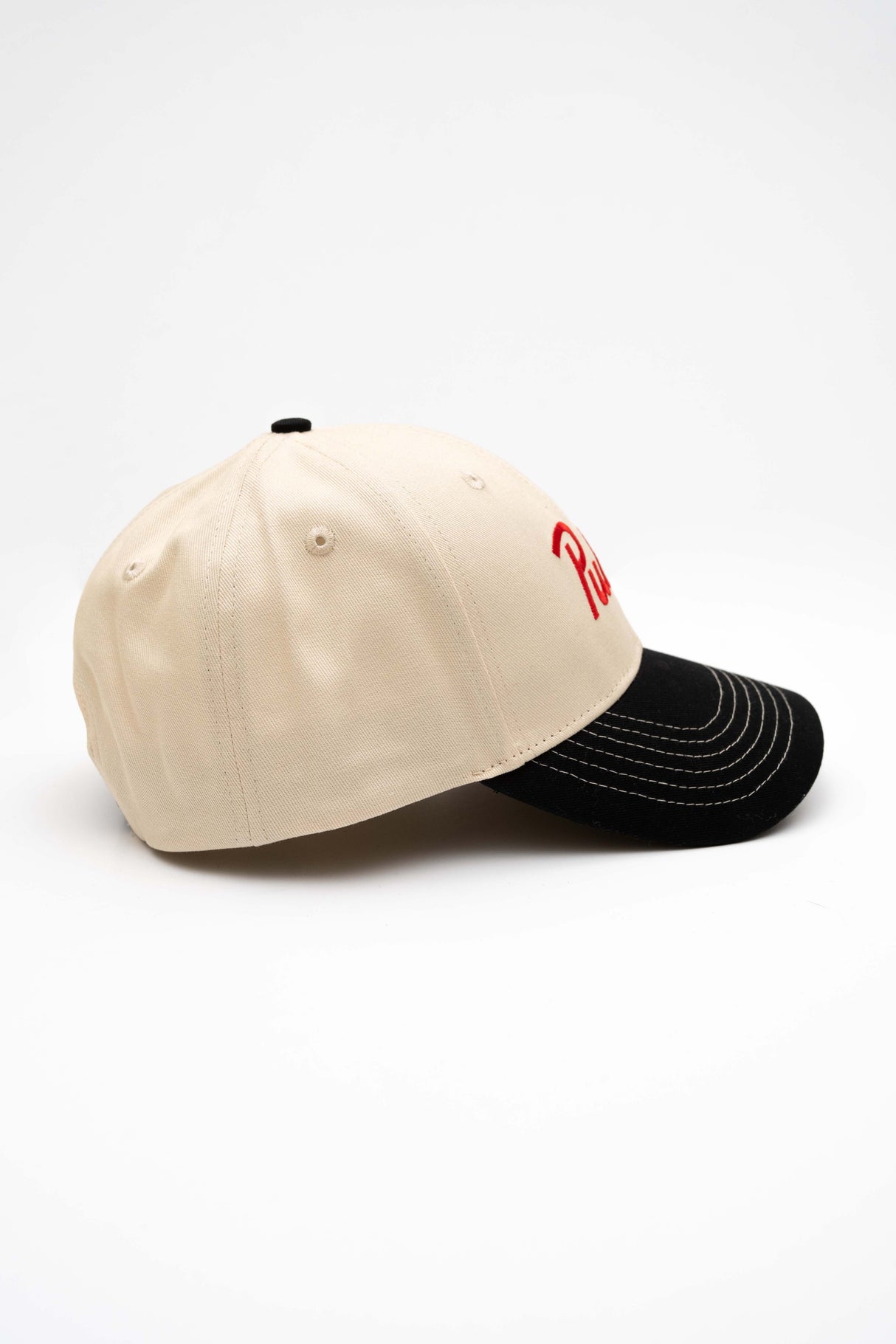 ScriptCap-A baseball cap with a cream-colored crown and a black curved brim, featuring the word 'Public' embroidered in red script on the front. The cap is photographed on a seamless white background.