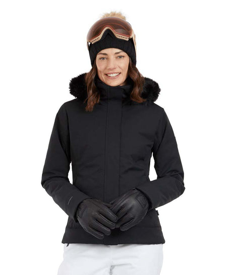 SolaceJacket-A woman wearing a black ski jacket with a faux-fur trimmed hood, black gloves, a black beanie, and ski goggles, posed against a solid white background.