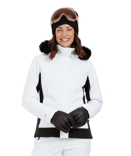 SolaceJacket-A woman wearing a white and black ski jacket with a black fur-trimmed hood, black gloves, a black beanie, and ski goggles, posed against a solid white background.