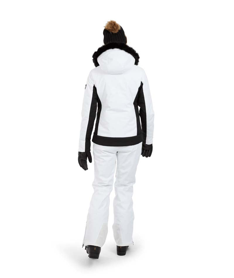 SolaceJacket-A woman wearing a white and black ski jacket with a black fur-trimmed hood, black gloves, a black beanie, and ski goggles, posed against a solid white background.