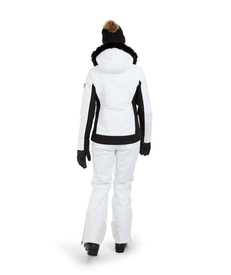 SolaceJacket-A woman wearing a white and black ski jacket with a black fur-trimmed hood, black gloves, a black beanie, and ski goggles, posed against a solid white background.