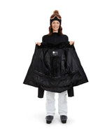 SolaceJacket-A woman wearing a black ski jacket with a faux-fur trimmed hood, black gloves, a black beanie, and ski goggles, posed against a solid white background.
