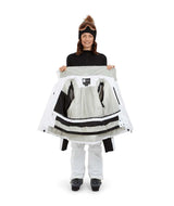 SolaceJacket-A woman wearing a white and black ski jacket with a black fur-trimmed hood, black gloves, a black beanie, and ski goggles, posed against a solid white background.