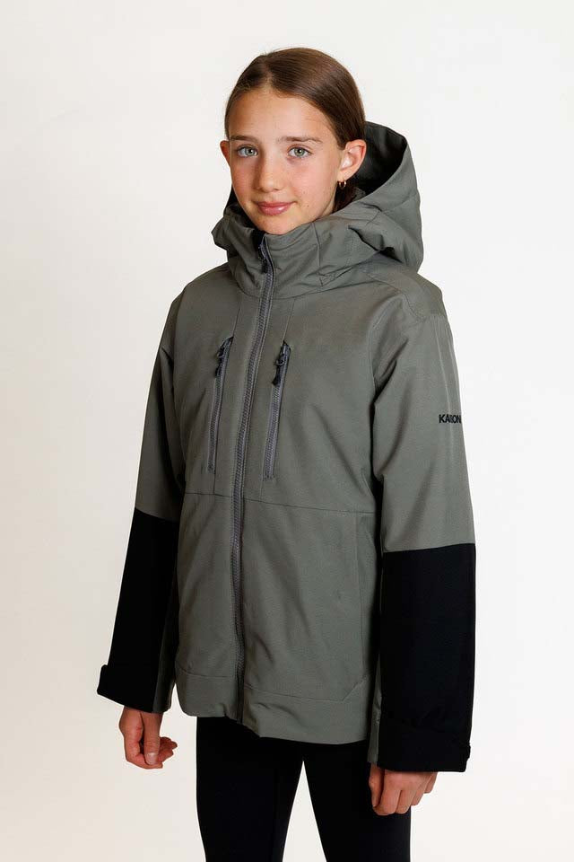 SquallKidsInsulatedJacket-A girl modeling a hooded ski jacket in a colorblock design of dark gray and black, with a small K2R logo on the left sleeve, shot against a plain white studio background.