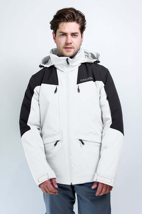 TritonMensInsulatedJacket-A man wearing a Karbon colorblock ski jacket in off-white and black, paired with gray pants, standing against a light gray studio background.