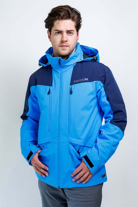 TritonMensInsulatedJacket-A man wearing a blue and navy Karbon ski jacket, standing against a light gray studio background.