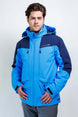 TritonMensInsulatedJacket-A man wearing a blue and navy Karbon ski jacket, standing against a light gray studio background.