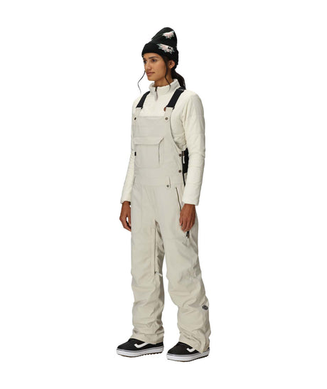 WBlackMagicInsulatedBib-Person wearing a white snowsuit and black beanie on a white background