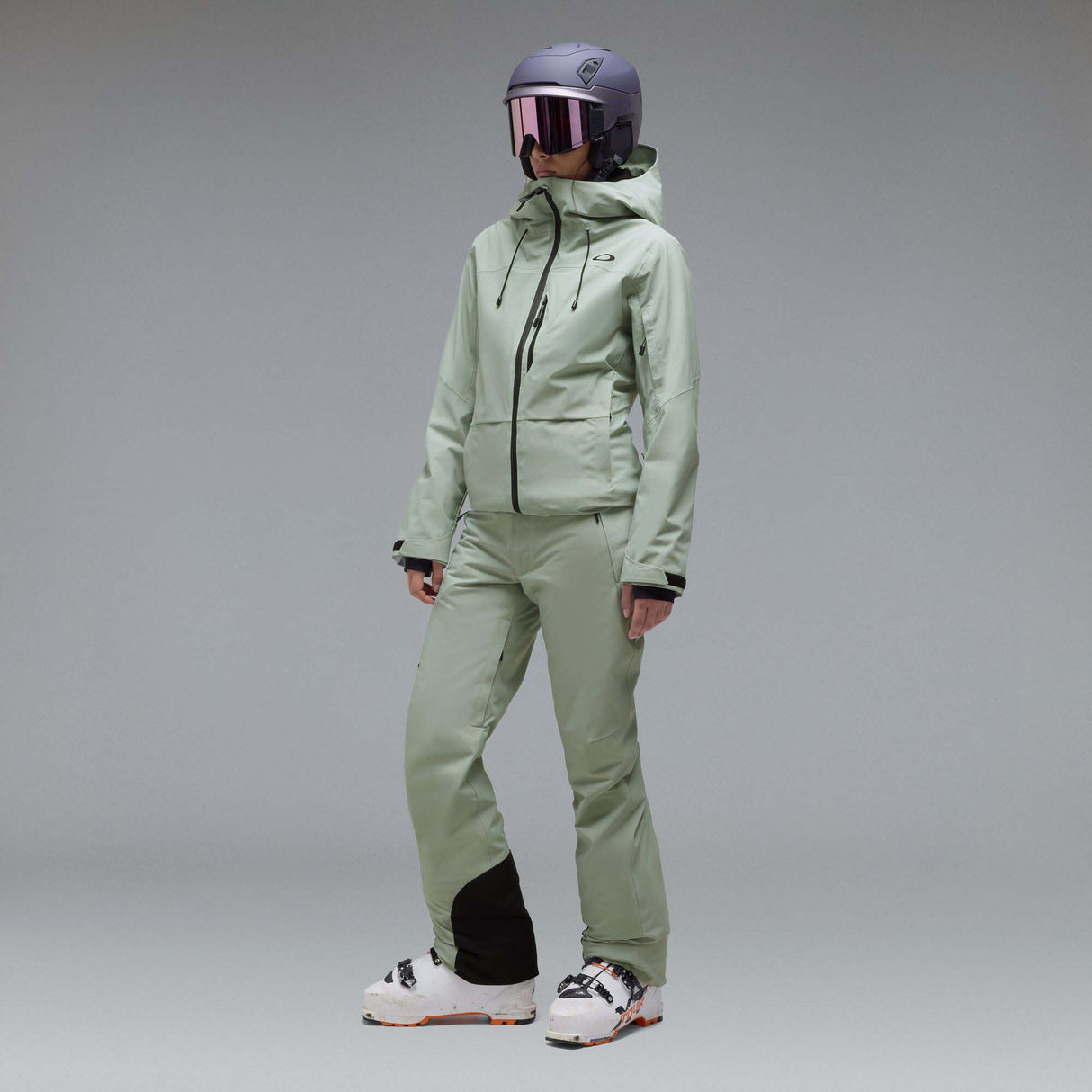WCanopyInsulatedJacket-A light sage green hooded jacket with black zipper and drawstring details, displayed on a neutral gray background. The Oakley logo is visible on the left chest.