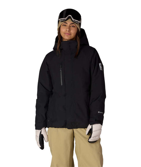 WGore-texWillowInsulatedJacket-Person wearing a black snow jacket, beige pants, and white gloves on a white background