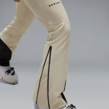 WIcicleSoftshellBib-A pair of ski bib pants in off-white with black suspenders, black zipper details, and black paneling at the lower legs, shown against a neutral gray gradient background.