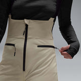 WIcicleSoftshellBib-A pair of ski bib pants in off-white with black suspenders, black zipper details, and black paneling at the lower legs, shown against a neutral gray gradient background.