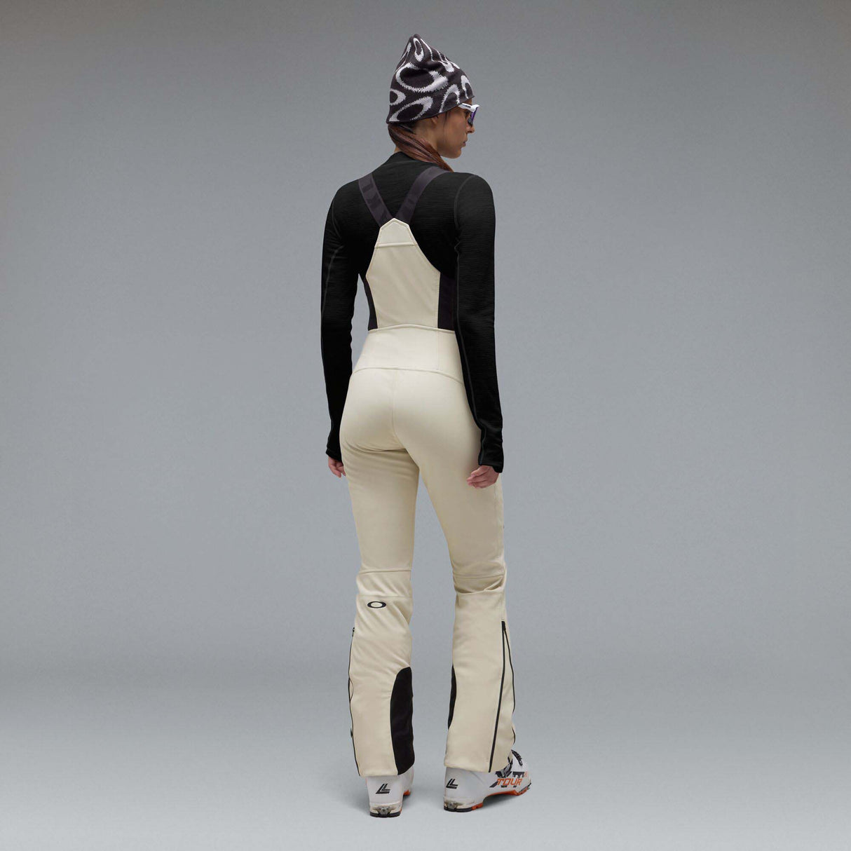 WIcicleSoftshellBib-A pair of ski bib pants in off-white with black suspenders, black zipper details, and black paneling at the lower legs, shown against a neutral gray gradient background.