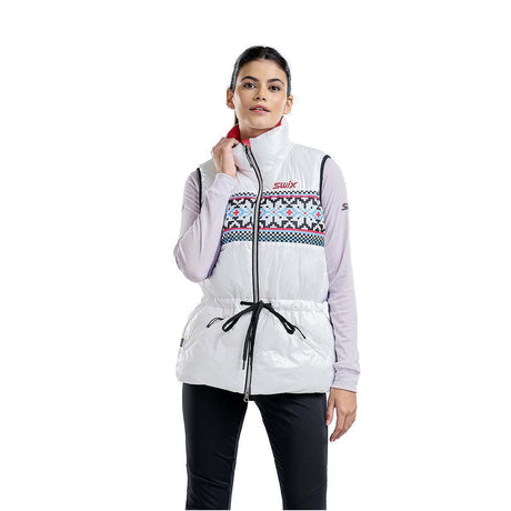 WMayenQuiltedPolyfillVest- A woman modeling a white sleeveless zip-front puffer vest with a colorful geometric pattern across the chest, black drawstring waist, and a red inner collar, worn over a light purple long-sleeve top and black pants against a white background.