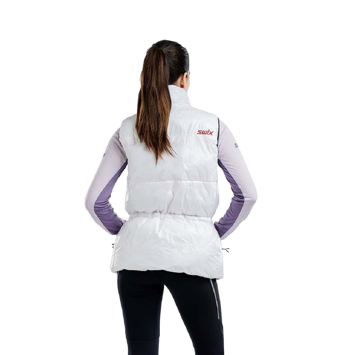 WMayenQuiltedPolyfillVest- A woman modeling a white sleeveless zip-front puffer vest with a colorful geometric pattern across the chest, black drawstring waist, and a red inner collar, worn over a light purple long-sleeve top and black pants against a white background.