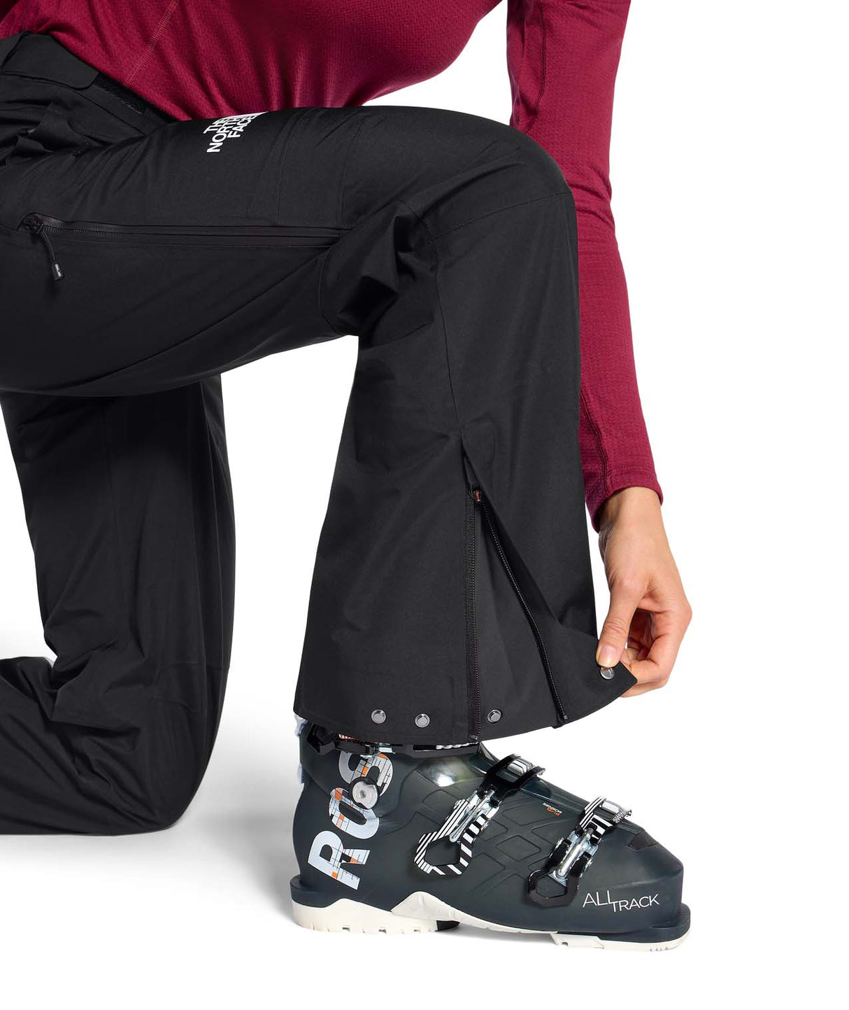 WSummitEastwallGTXPant-Person wearing black ski pants and a maroon top, adjusting a ski boot on a white background.
