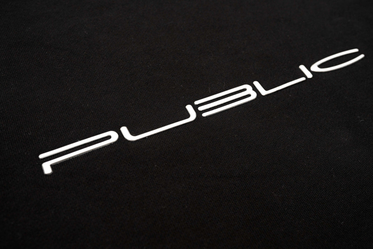 WarpCrewneck-A close-up of a black textured surface featuring the word 'PUBLIC' in a stylized white sans-serif font.