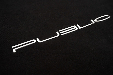 WarpCrewneck-A close-up of a black textured surface featuring the word 'PUBLIC' in a stylized white sans-serif font.