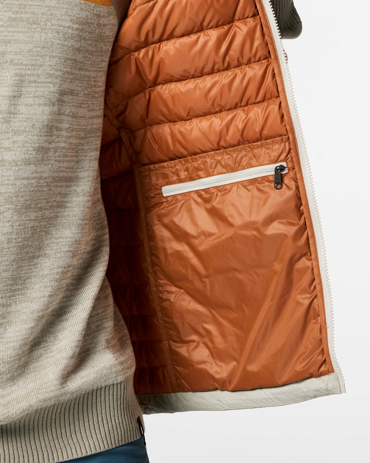 m-fuego-down-vest- A quilted puffer vest by Cotopaxi in a light beige color, featuring horizontal quilting, a full-zip front, and a mock neck collar. It has a distinctive color-blocked chest design with horizontal stripes of dark teal, rust orange, and golden yellow, with the Cotopaxi logo printed on the chest.