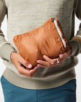 m-fuego-down-vest- A quilted puffer vest by Cotopaxi in a light beige color, featuring horizontal quilting, a full-zip front, and a mock neck collar. It has a distinctive color-blocked chest design with horizontal stripes of dark teal, rust orange, and golden yellow, with the Cotopaxi logo printed on the chest.