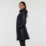 w-fuego-down-parka-A woman modeling a long, black quilted puffer jacket with a hood and a small embroidered 'Cotopaxi' logo on the left chest, set against a plain light gray studio background.
