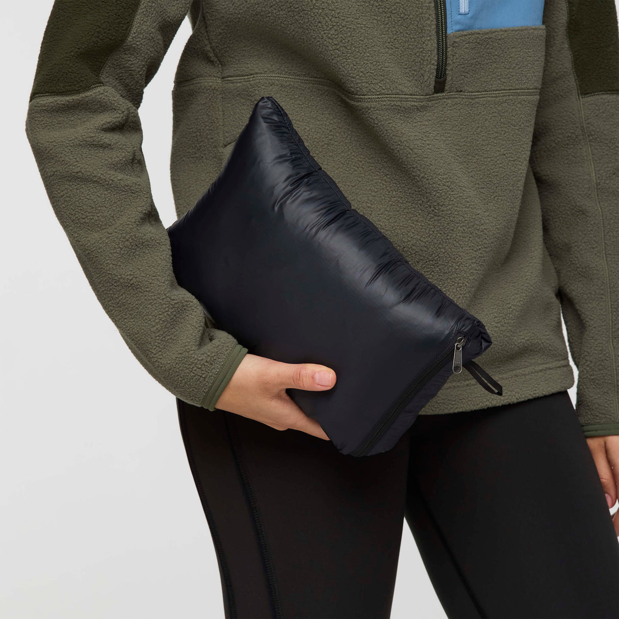 w-fuego-down-parka-A woman modeling a long, black quilted puffer jacket with a hood and a small embroidered 'Cotopaxi' logo on the left chest, set against a plain light gray studio background.